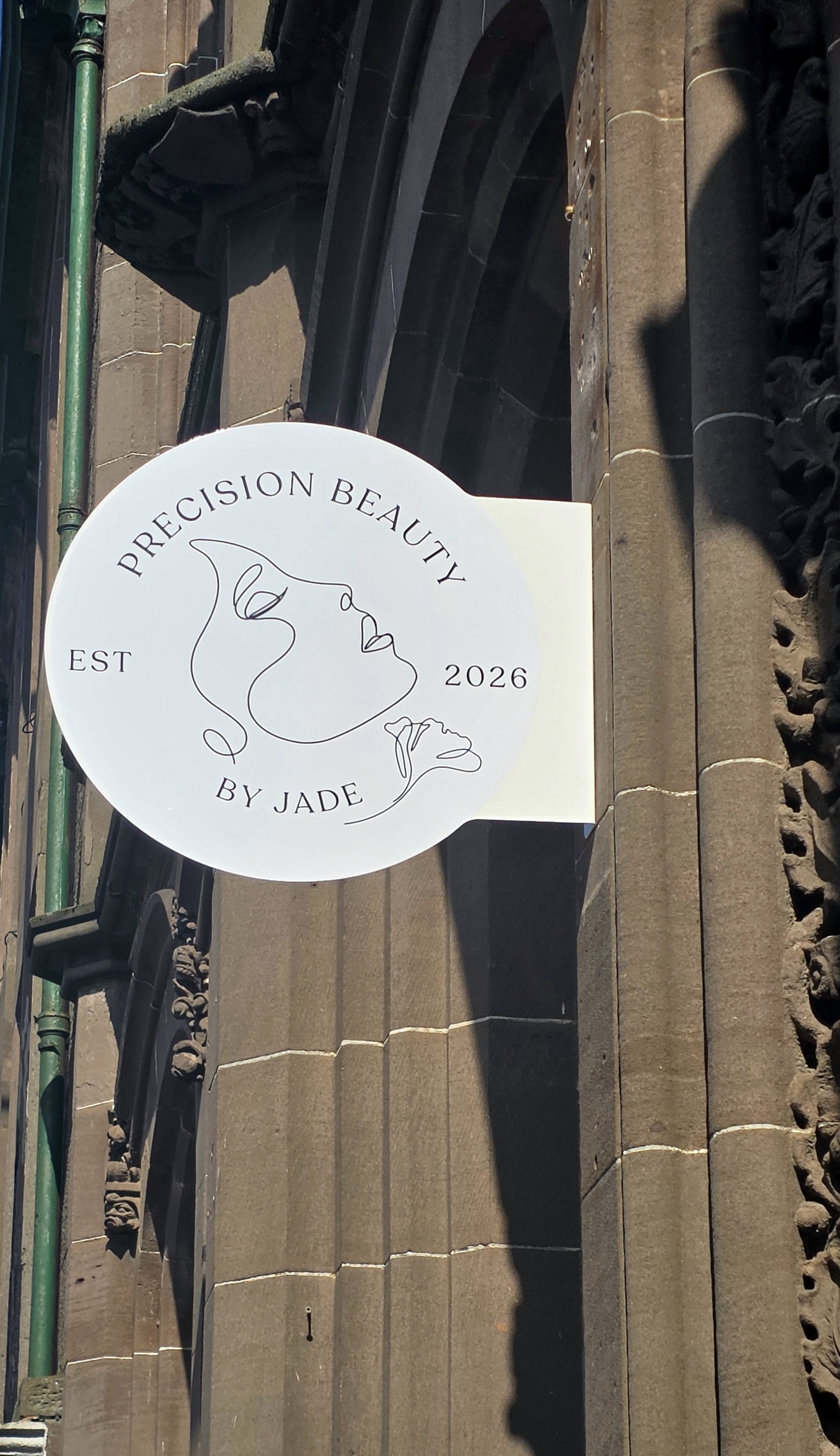 The round Precision Beauty By Jade hanging sign on the sandstone front of 14 Castle Place
